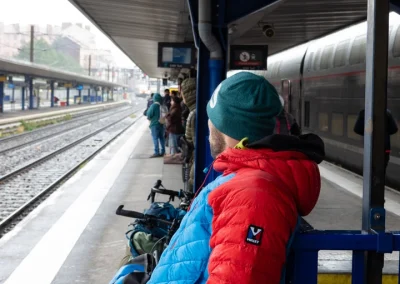 Un homme avec une doudoune bleu et rouge attend le train - © Florian Garibal